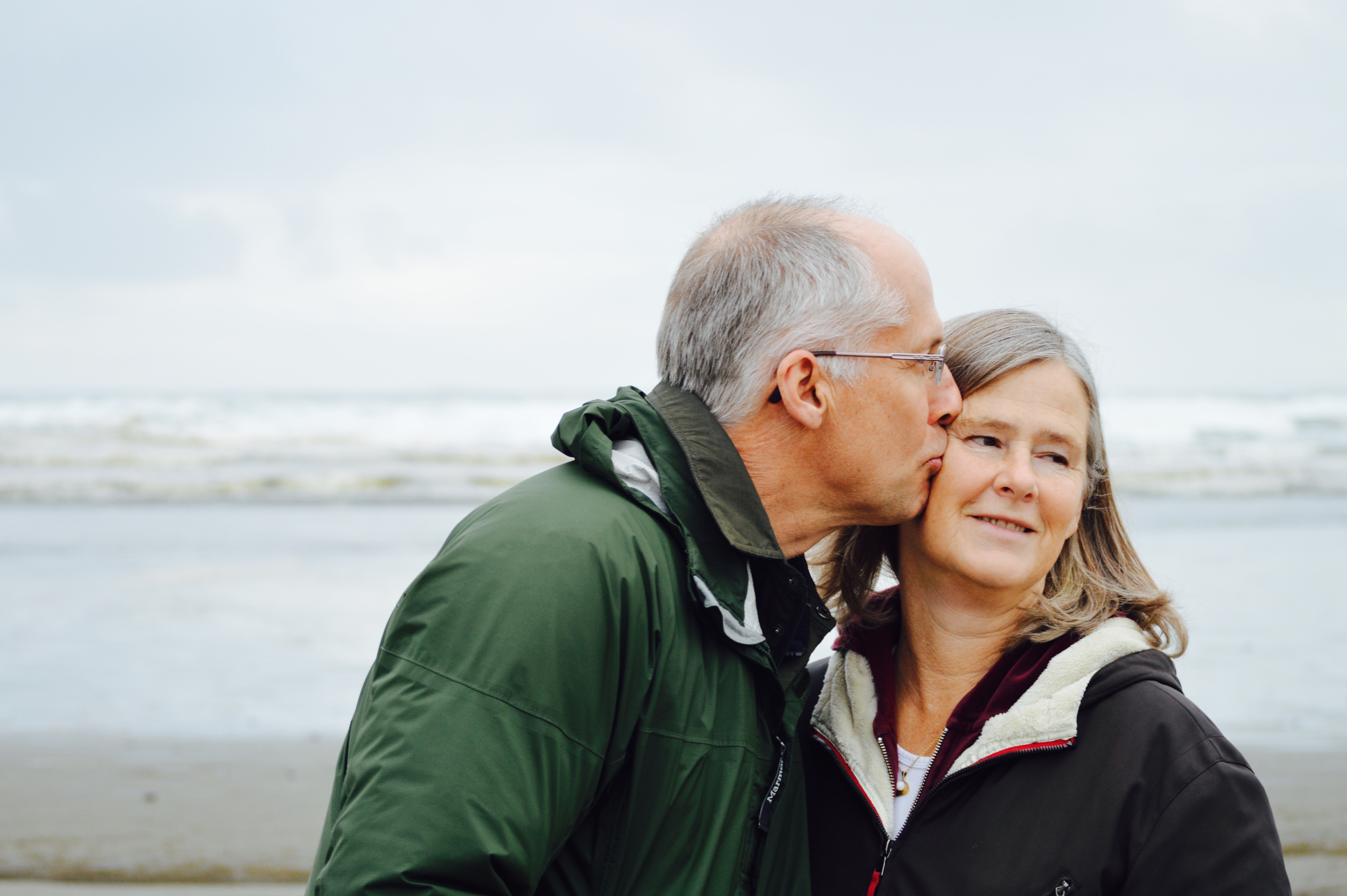 En man pussar kvinnan på kinden medan de står på en strand
