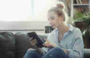 En kvinna sitter i soffan och läser från sin mobil