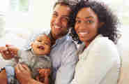 Ett man, kvinna och deras bebis ler mot kameran