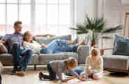 En man och en kvinna som sitter i en soffa medans deras barn leker på golvet