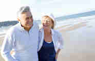 Ett äldre par skrattar och går längst med en strand