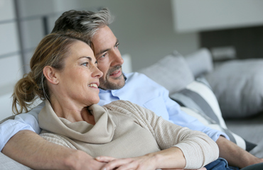 Ett par sitter i soffan och mannen har sin arm runt kvinnans axlar