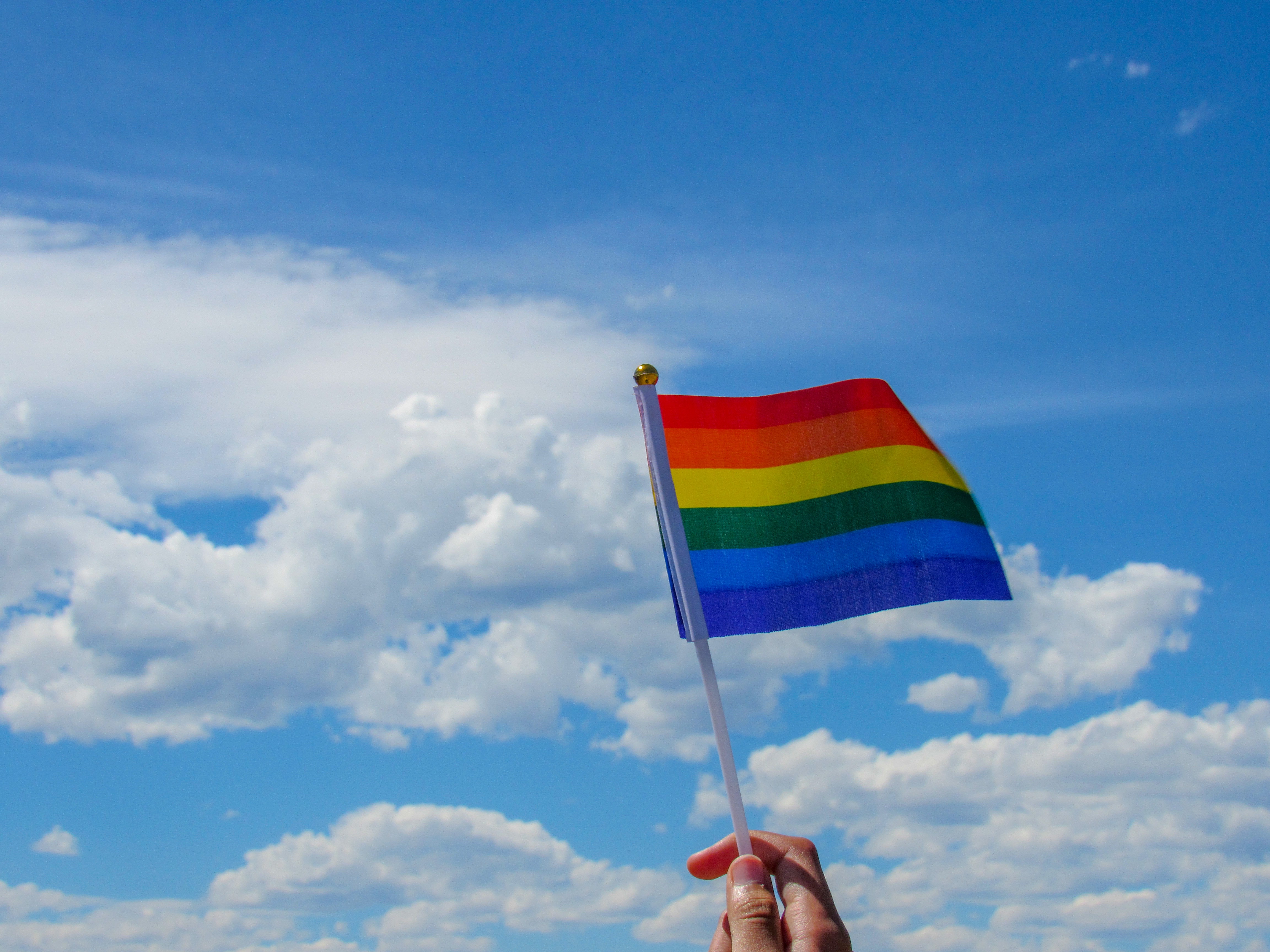 En himmel med där en hand håller upp regnbågsflaggan