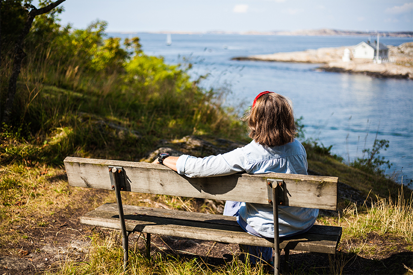 En kvinna sitter på en bänk och blickar ut över havet