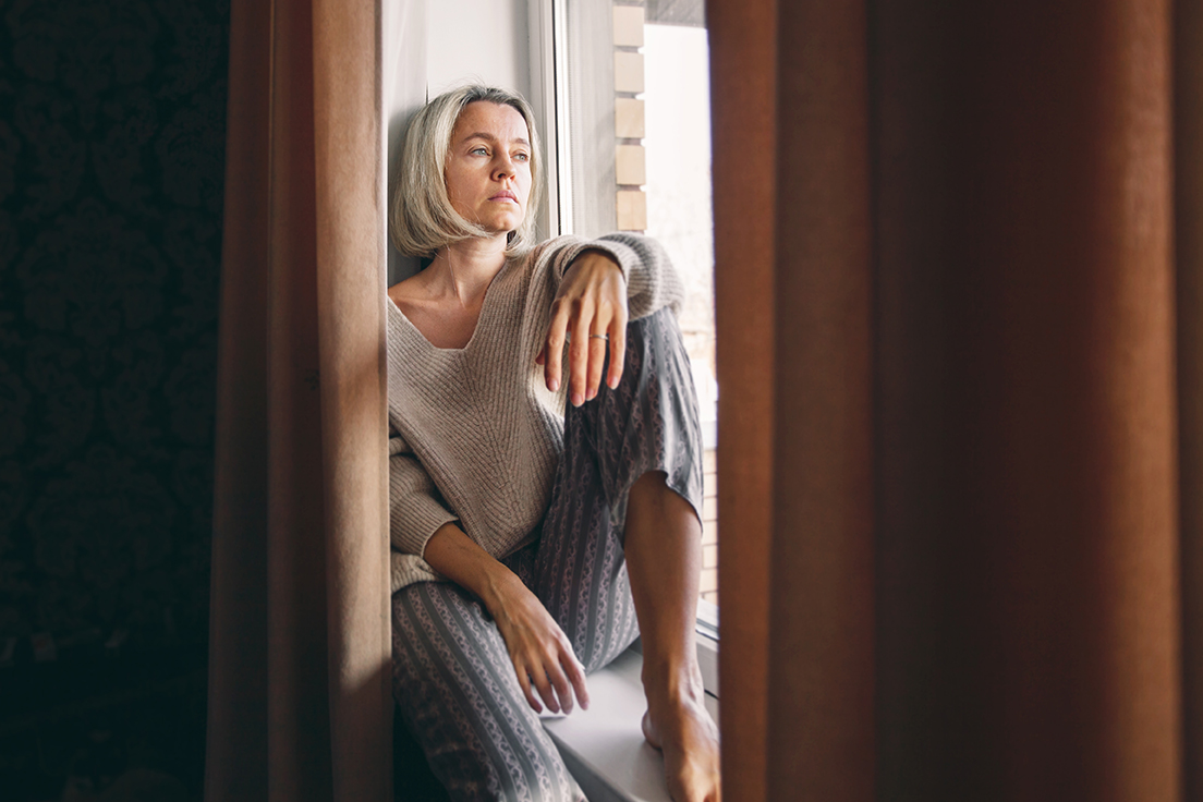 En ledsen kvinna sitter i ett fönster