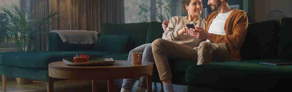 Par som sitter i soffa och tittar på en mobil tillsammans