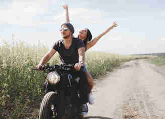 En man och en kvinna åker motorcykel och kvinnan har händerna uppe i luften